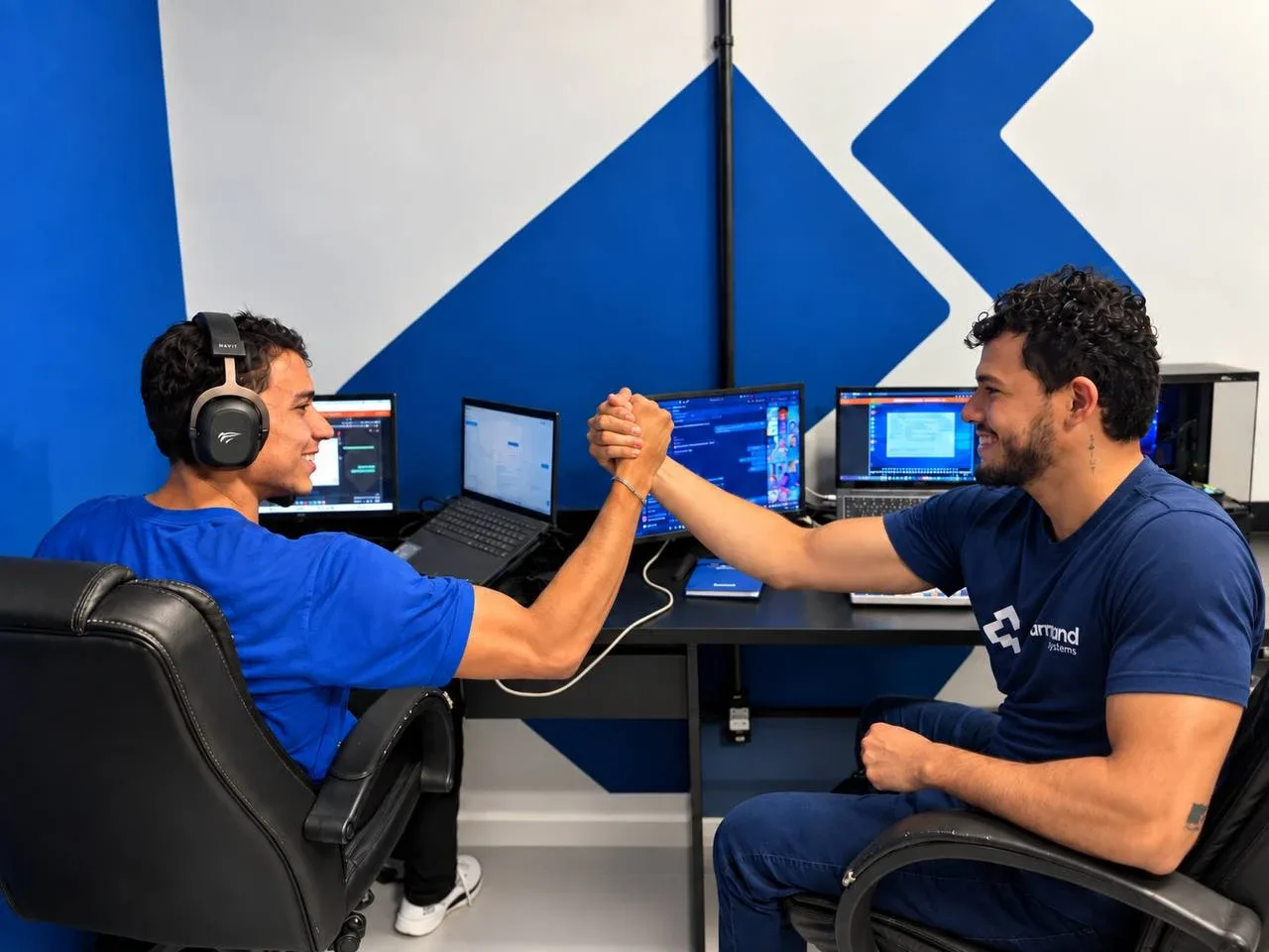Dois colaboradores da Command System apertando as mãos em frente à parede azul com o símbolo da marca